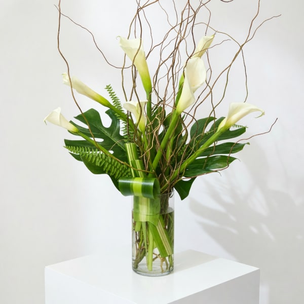 White calla lilies in a clear glass vase with curly branches