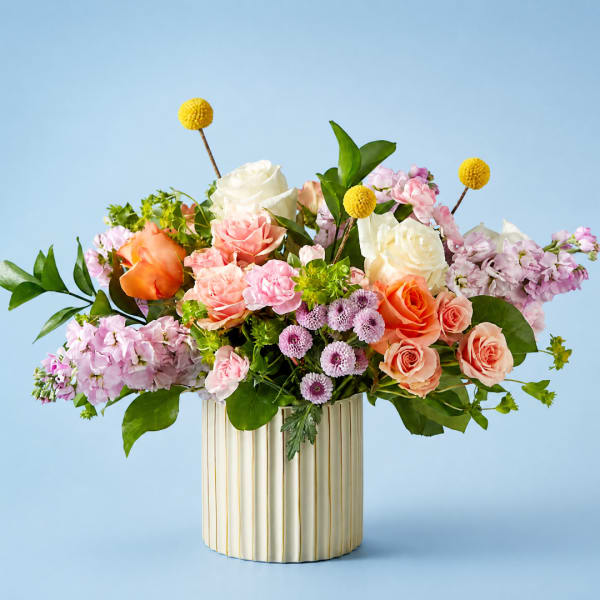 Mixed bouquet of roses and pink flowers in a ribbed cream vase