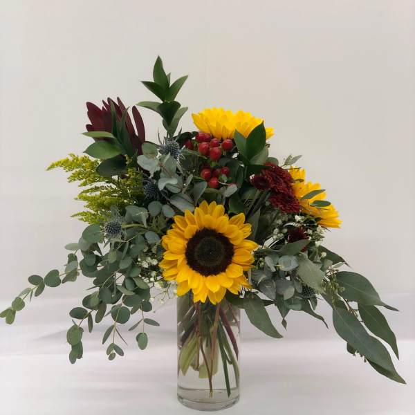 Sunflower arrangement in a clear glass vase with mixed greenery and red berries
