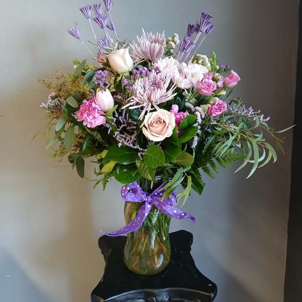 Mixed pink and lavender bouquet in a glass vase with a purple ribbon.