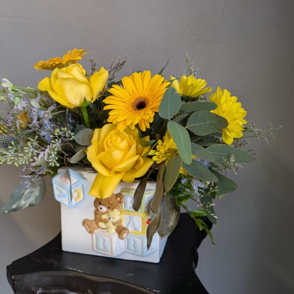 Yellow roses and daisies in a baby-themed ceramic vase