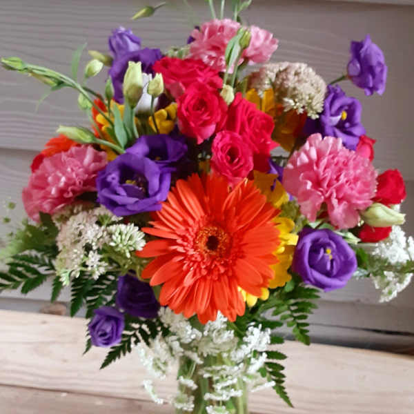 Colorful mixed bouquet in a clear glass vase with orange, pink, purple, and white blooms