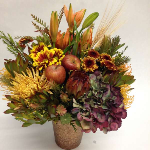 Autumn bouquet with lilies, chrysanthemums, apples, and hydrangea in a textured vase