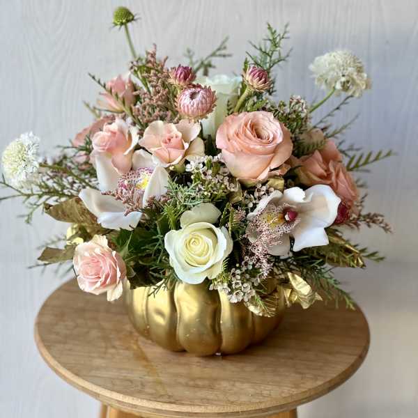 Pink and white floral arrangement in a gold pumpkin vase