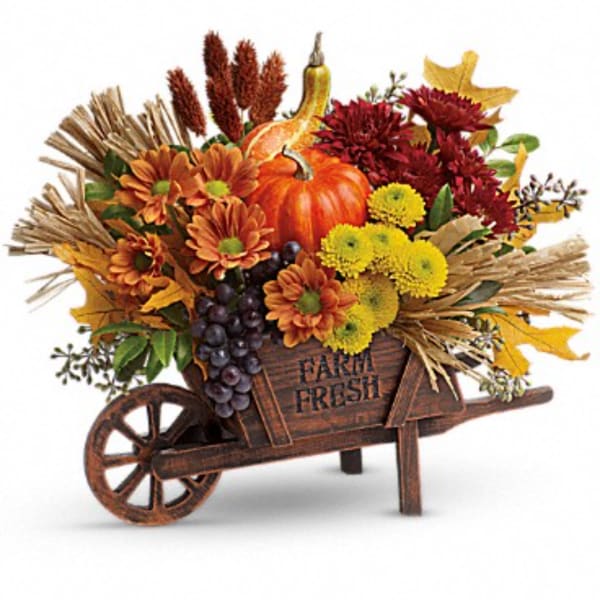 Fall floral arrangement in a wooden wheelbarrow with pumpkins and mums