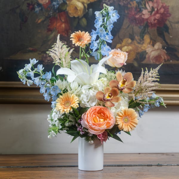 Mixed bouquet in a white vase with lilies, gerberas, roses, and blue delphinium