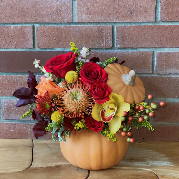 Fall floral arrangement in a pumpkin container with red roses and yellow orchid