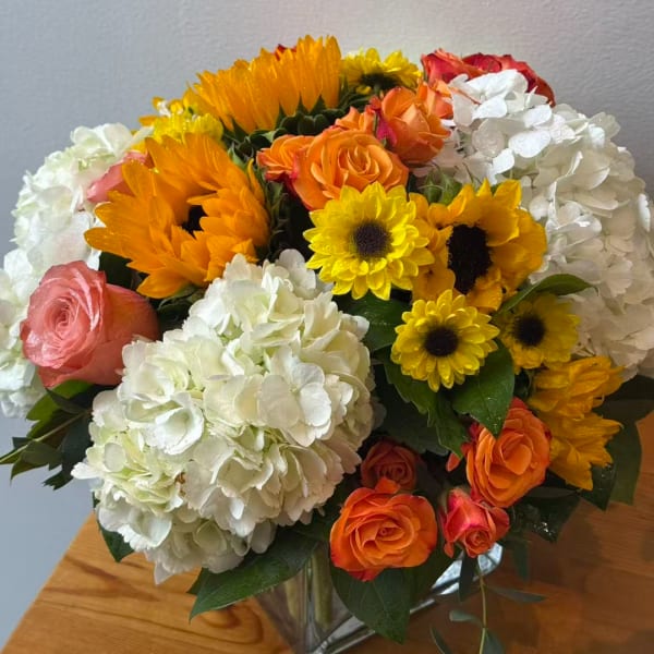 Bouquet of orange and pink roses with white hydrangeas and yellow sunflowers in a glass vase
