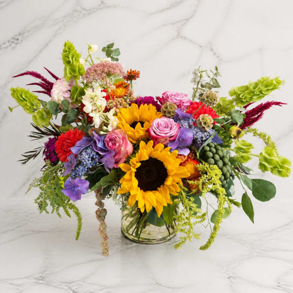 Colorful mixed bouquet in a clear glass vase with sunflowers and roses