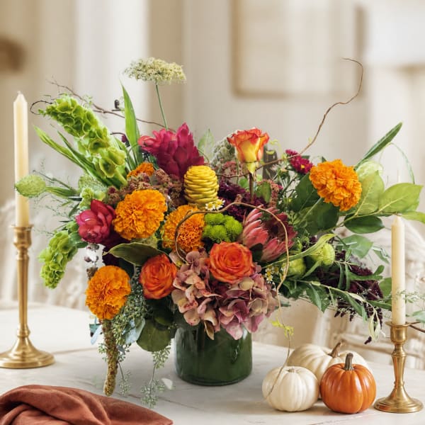 Colorful autumn floral arrangement in a green vase with pumpkins nearby