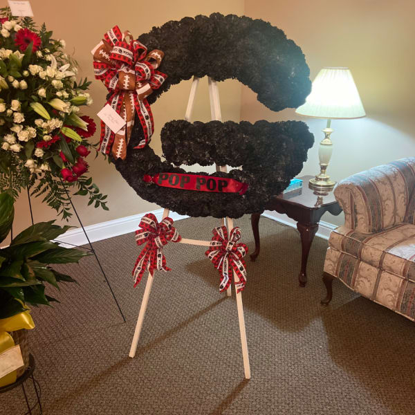 Football-shaped floral tribute on an easel with red-and-white ribbons