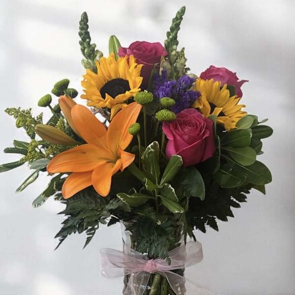 Mixed bouquet with sunflowers, roses, and an orange lily in a glass vase