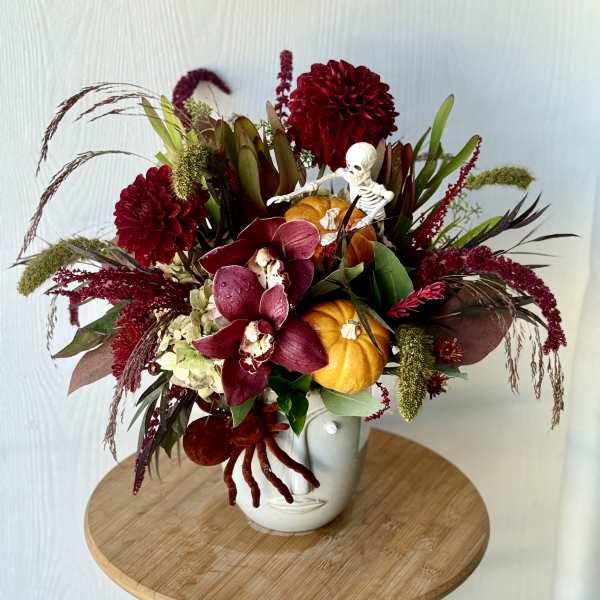Autumn floral arrangement with burgundy blooms, orchids, and small pumpkins in a white vase
