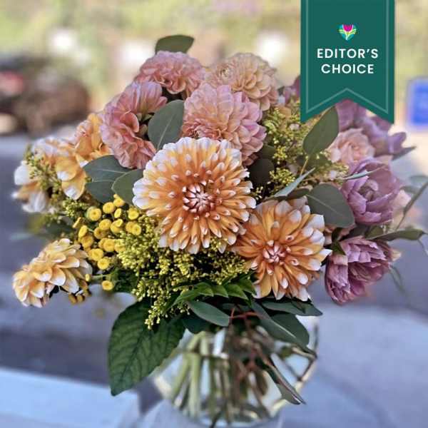 Peach dahlias and yellow filler flowers arranged in a clear glass vase