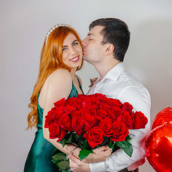 Couple holding a large bouquet of red roses with red heart balloons