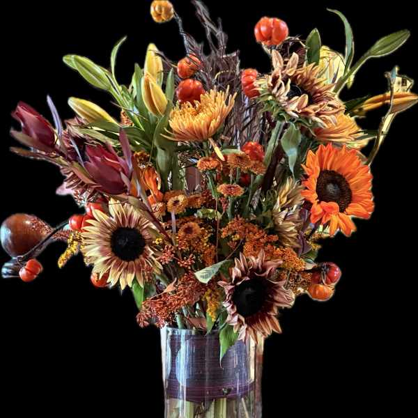 Autumn bouquet with sunflowers and orange blooms in a clear glass vase