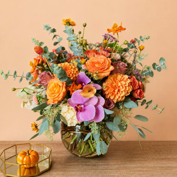 Mixed orange and purple flower arrangement in a glass vase with eucalyptus