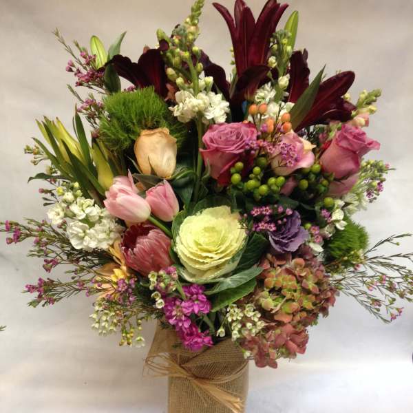 Mixed bouquet with lilies, roses, tulips, and hydrangea in a burlap-wrapped vase