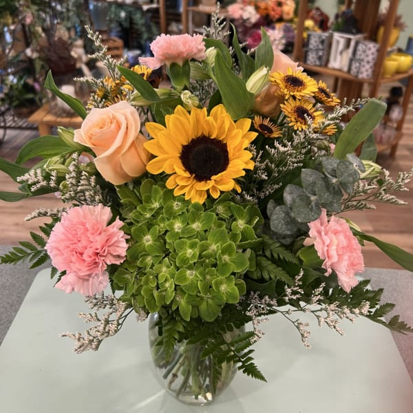 Mixed bouquet with sunflowers, peach roses, pink carnations, and a glass vase