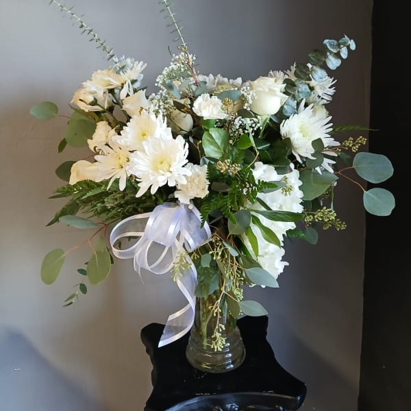 White flowers in a glass vase with a white ribbon