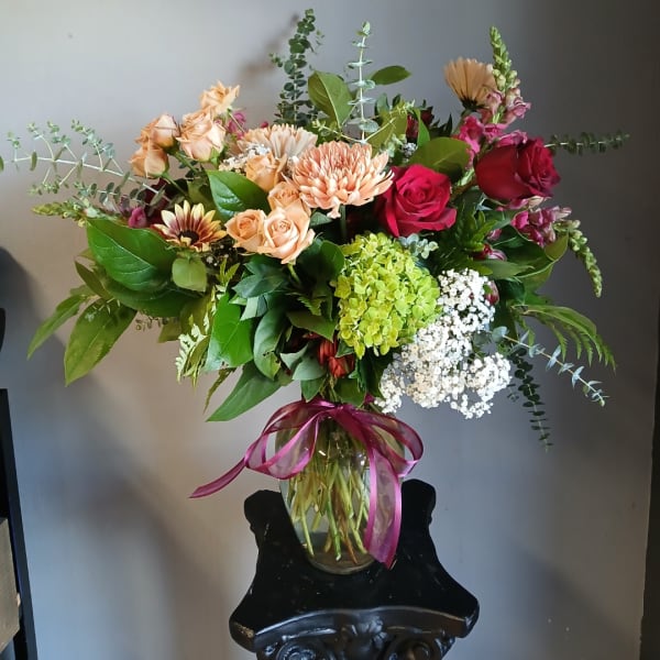 Mixed bouquet of roses, chrysanthemums, and hydrangea in a glass vase with a ribbon