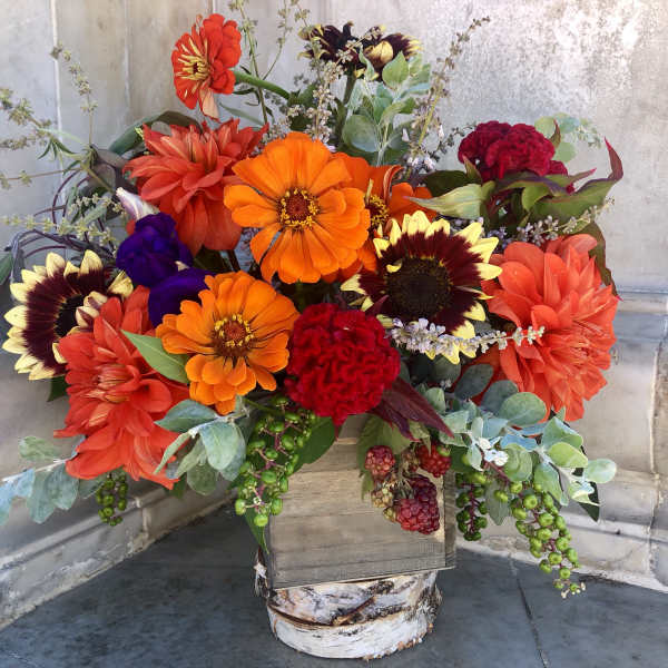 Bright mixed bouquet with orange, red, and purple flowers in a rustic wooden container