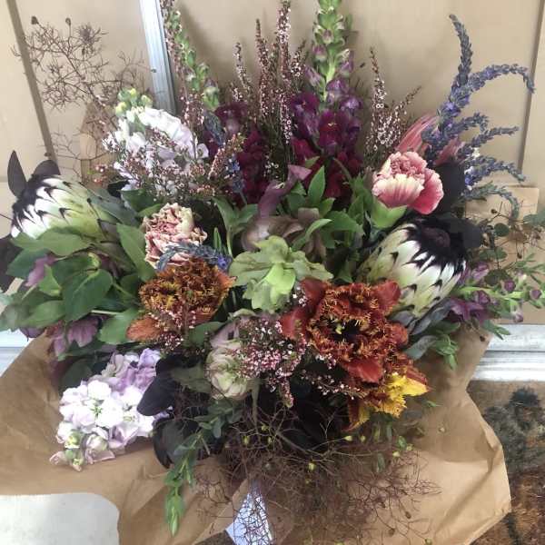 Large mixed bouquet with purple, pink, white, and orange blooms wrapped in brown paper