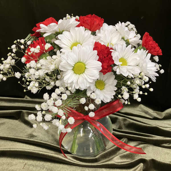 Red carnations and white daisies with baby's breath in a round glass vase with red ribbon