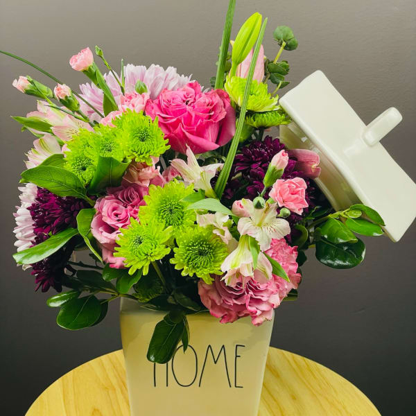 Pink and green mixed bouquet in a white container labeled HOME