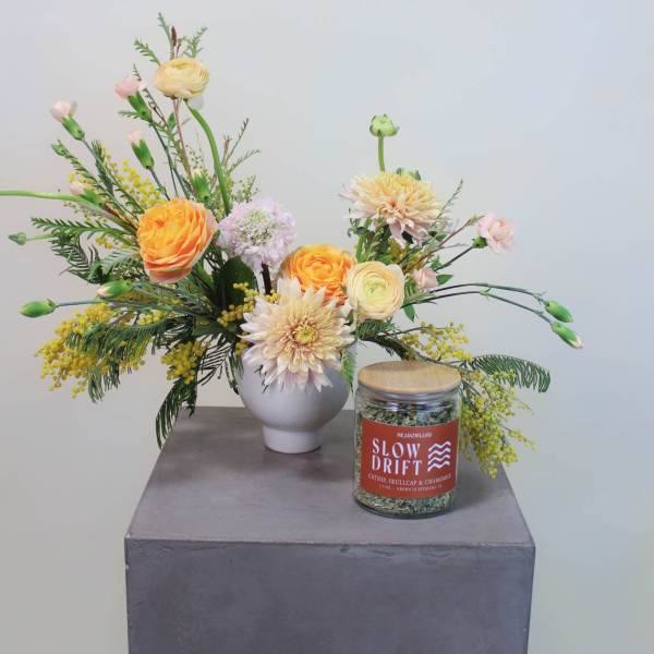 Mixed floral arrangement in a white vase with a jar candle beside it
