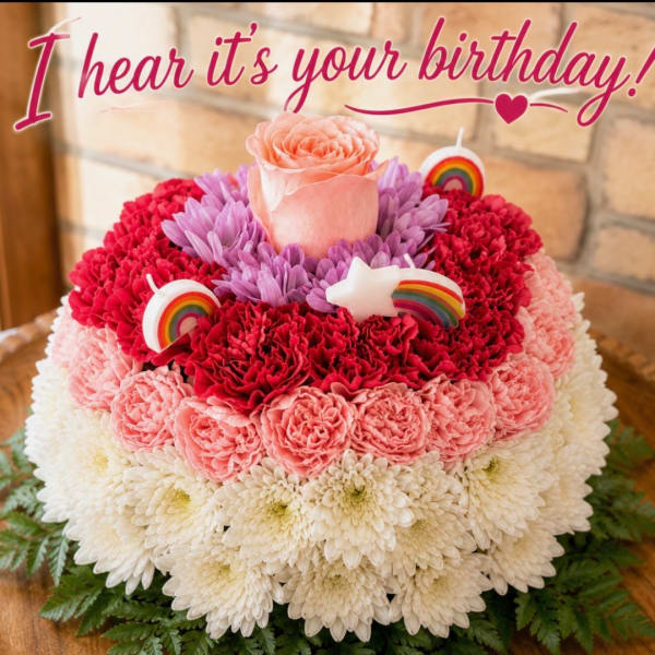 Round floral cake with pink, red, and white blooms and birthday topper