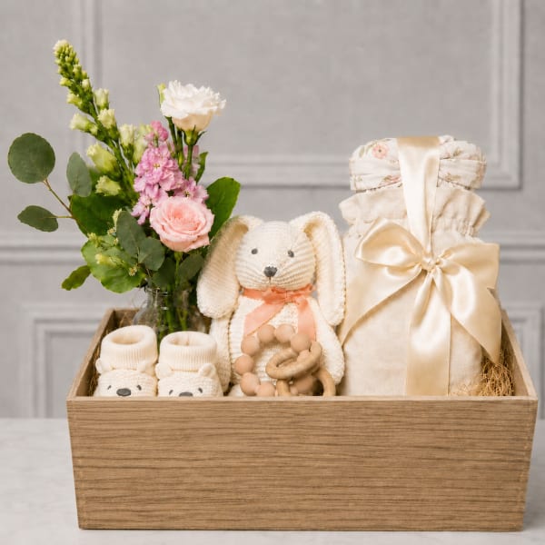 Gift basket with a small flower arrangement, baby clothes, and a plush bunny