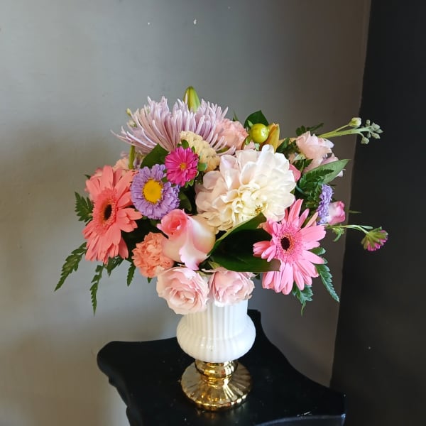 Mixed pastel flower arrangement in a white vase with gold base