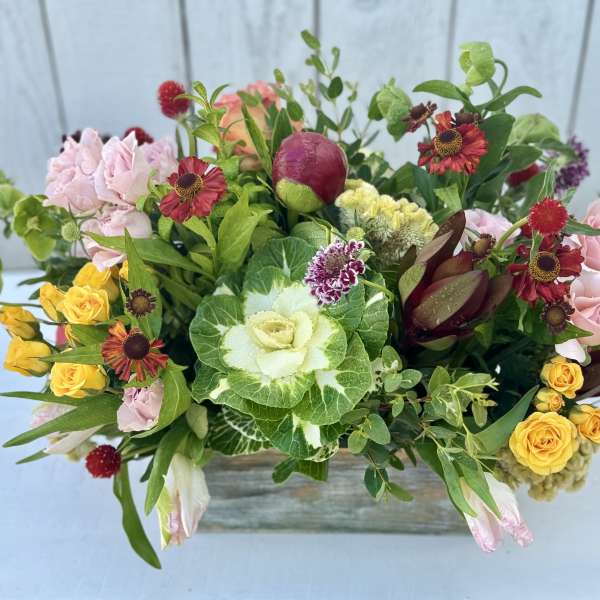 Mixed bouquet with pink and yellow roses in a low wooden container