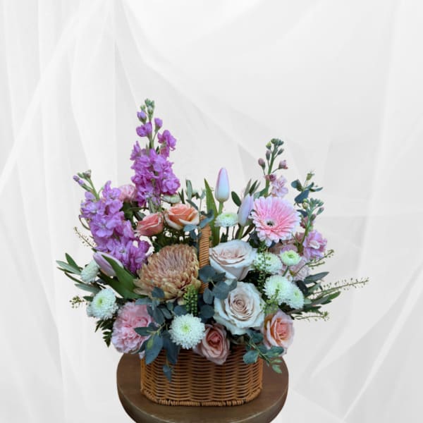 Mixed pink and purple flower arrangement in a wicker basket