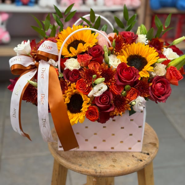 Mixed bouquet with sunflowers, red roses, and orange blooms in a pink gift box