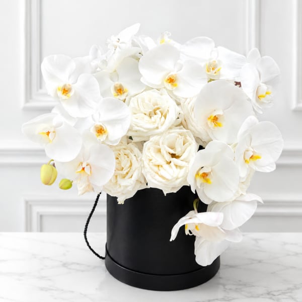 White orchids and cream roses arranged in a black hatbox