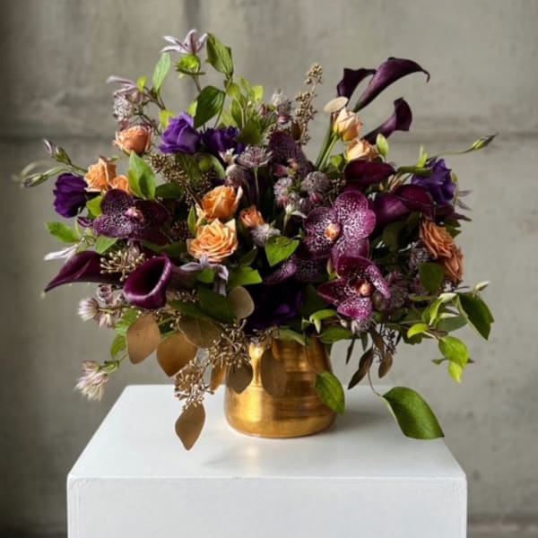 Mixed bouquet of purple, peach, and burgundy flowers in a gold vase