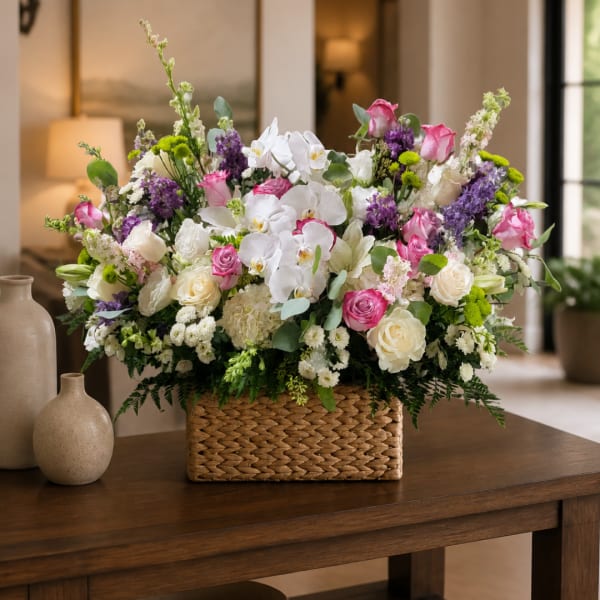 Mixed bouquet in a woven basket with white orchids, pink roses, and purple flowers