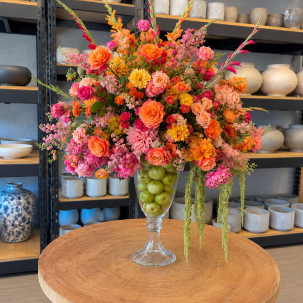 Colorful flower arrangement in a clear glass vase filled with green apples