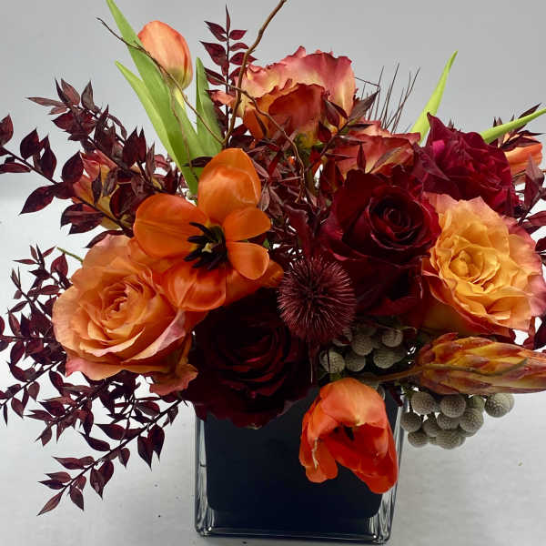 Orange and red roses with tulips in a square glass vase