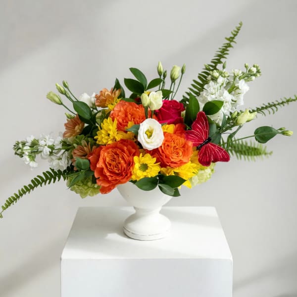 Colorful bouquet in a white pedestal vase with orange, yellow, red, and white blooms