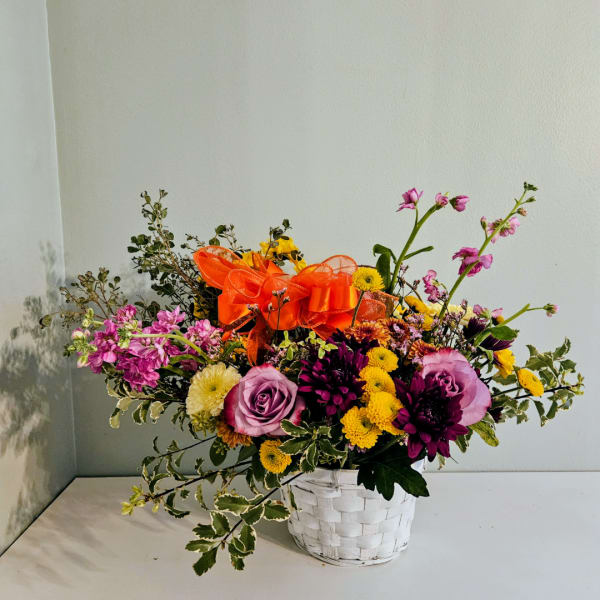 Mixed bouquet in a white woven basket with an orange ribbon