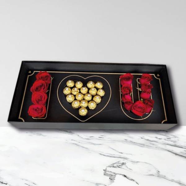 Black gift box with red roses and gold-wrapped chocolates arranged in a heart