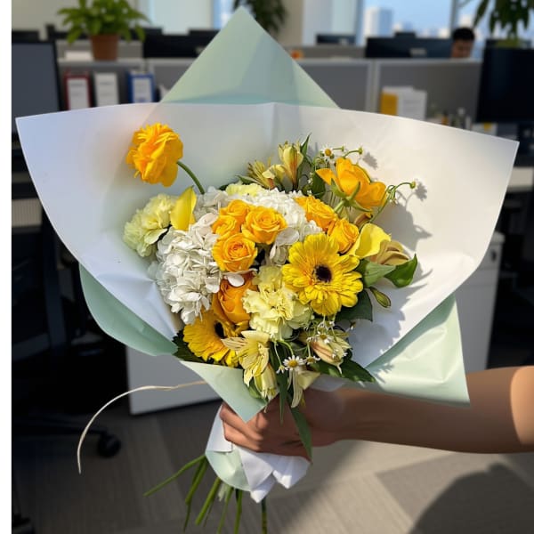 Handheld bouquet of yellow and white flowers wrapped in pale paper