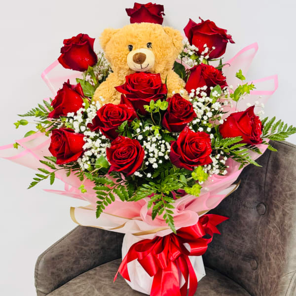 Bouquet of red roses with a teddy bear and pink wrapping
