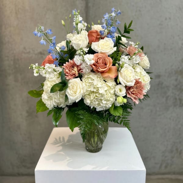 Wedding bouquet in a glass vase with white, peach, and blue flowers
