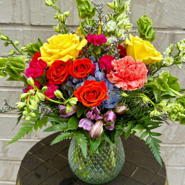 Colorful bouquet of roses, carnations, and other blooms in a textured glass vase