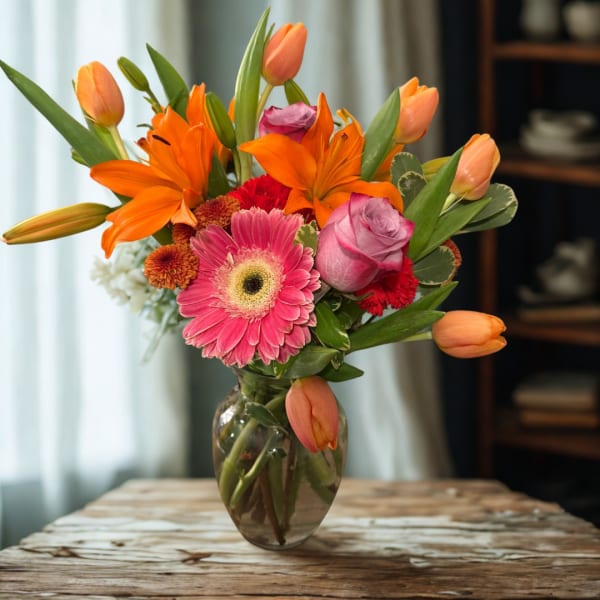 Mixed bouquet of orange lilies, pink gerbera daisies, and roses in a glass vase