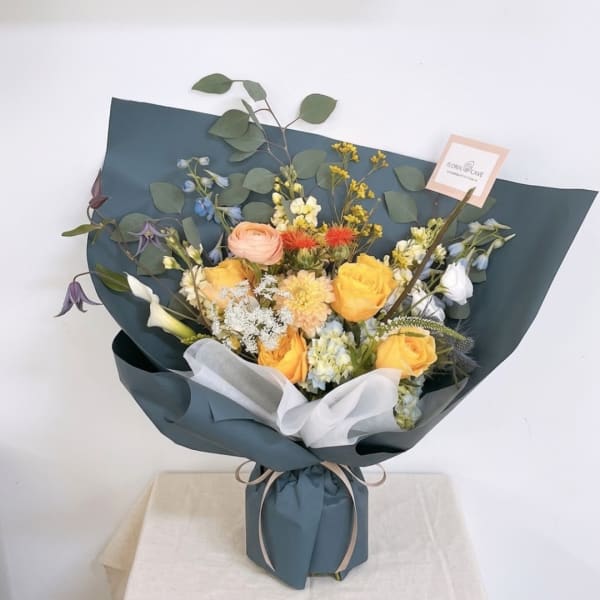 Mixed bouquet of yellow and peach flowers wrapped in dark blue paper